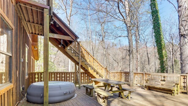 Une terrasse en bois avec un jacuzzi, des tables de pique-nique et un escalier en bois menant à un niveau supérieur.