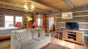 A cozy log cabin interior with a sofa, television, wooden cabinet, and a chandelier.