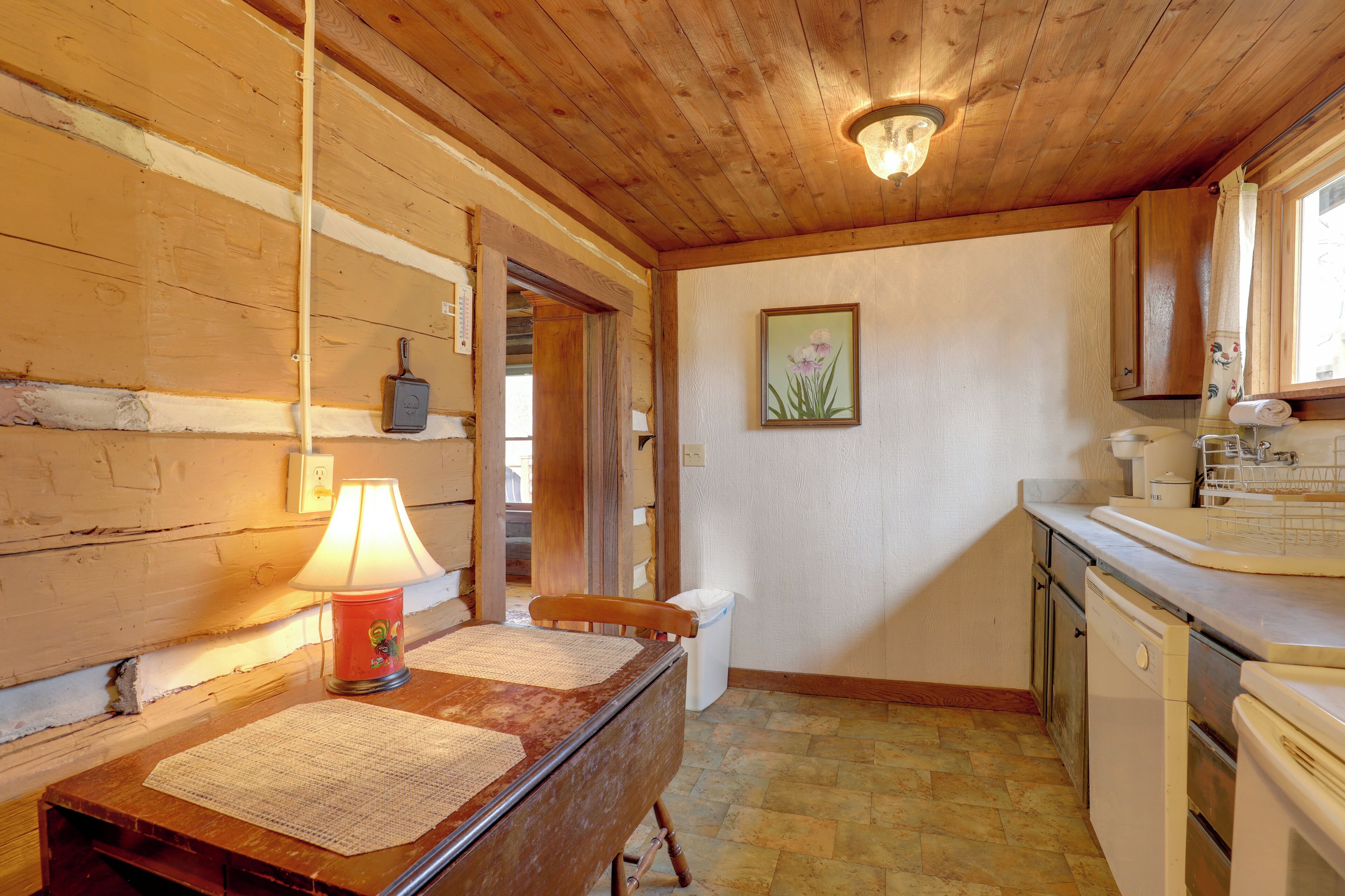 A wooden interior with a table, lamp, and kitchen area including a sink and cabinets.