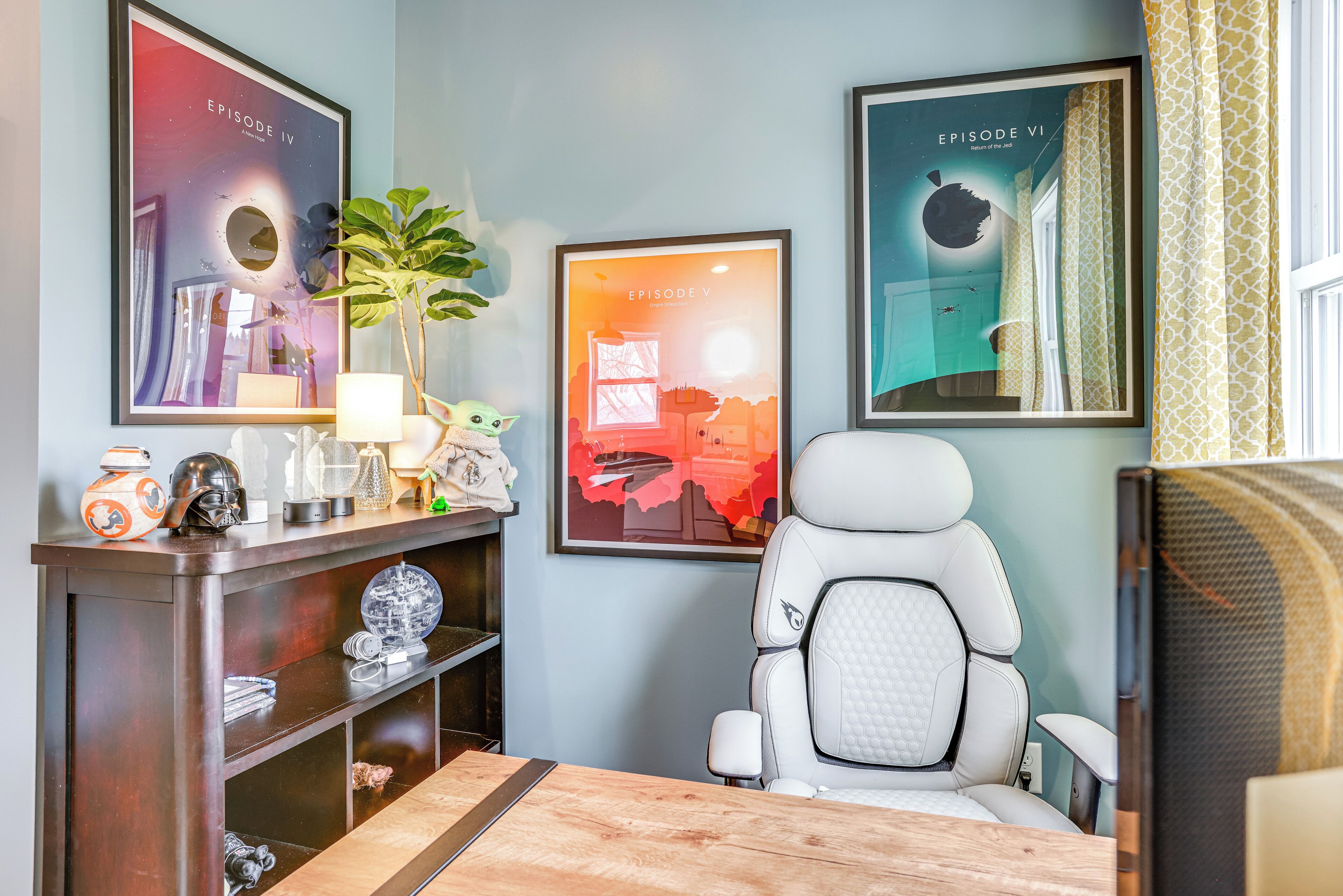 Una habitación con una silla gamer blanca, un escritorio de madera y una estantería con recuerdos de Star Wars.