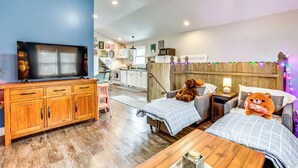 A cozy room with a TV, wooden furniture, a bed with a teddy bear, and a kitchen in the background. - Close to Trails & Town! Artsy Apt in Frankfort (Frankfort)
