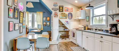 Una cocina con armarios blancos, un comedor con mesa y sillas, y varias decoraciones de pared, incluyendo cuadros enmarcados y letreros de neón.