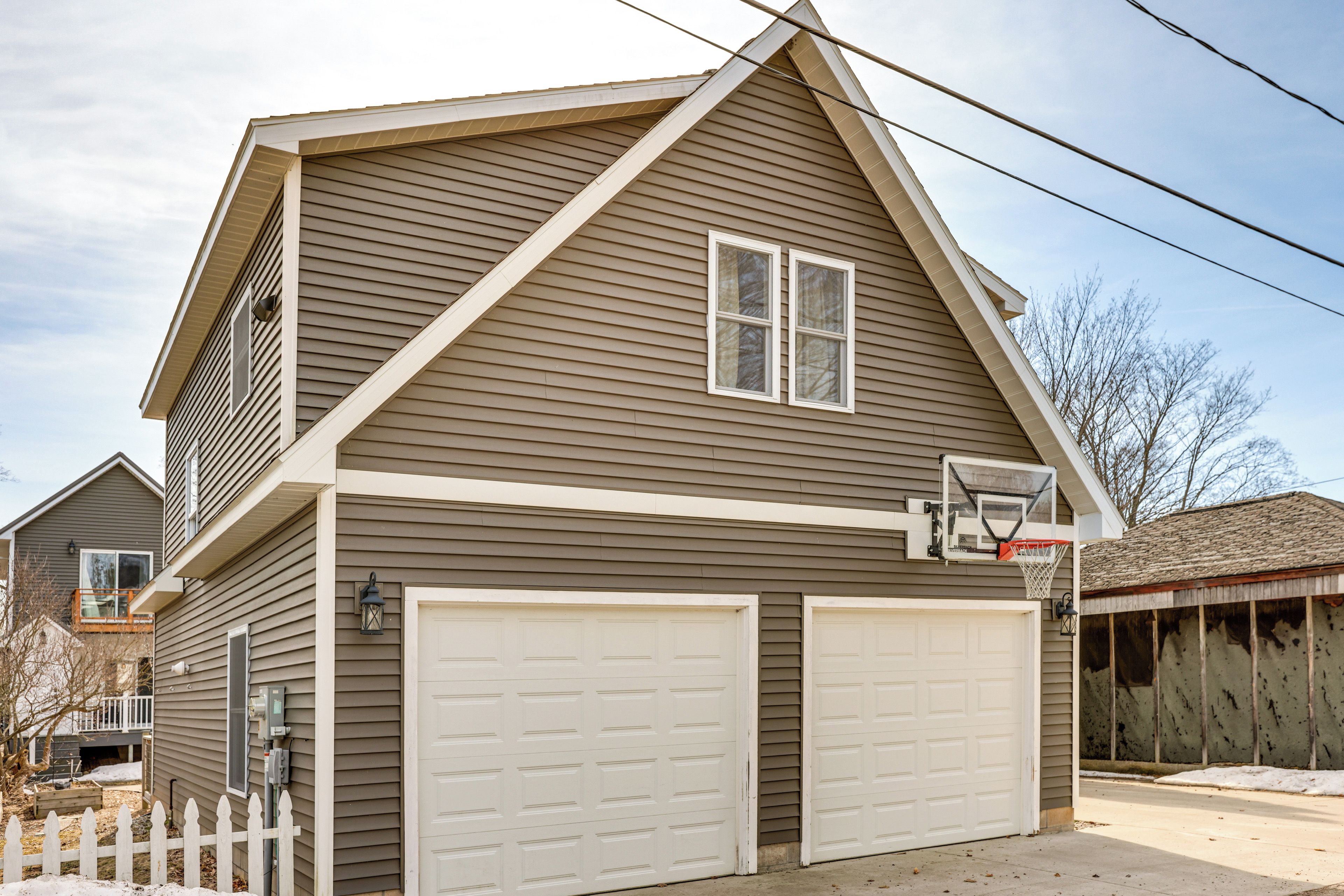 Ein zweigeschossiges Haus mit Garage, Basketballkorb und weißem Zaun.