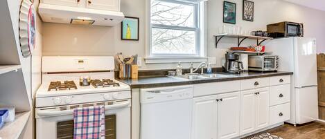 A modern kitchen with white cabinetry, a stove, a dishwasher, and a microwave. There is a window providing natural light and a patterned rug on the floor.