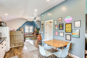 Un coin repas avec une table en bois et des chaises bleu clair, une cuisine avec un réfrigérateur blanc et un escalier menant à un autre niveau.