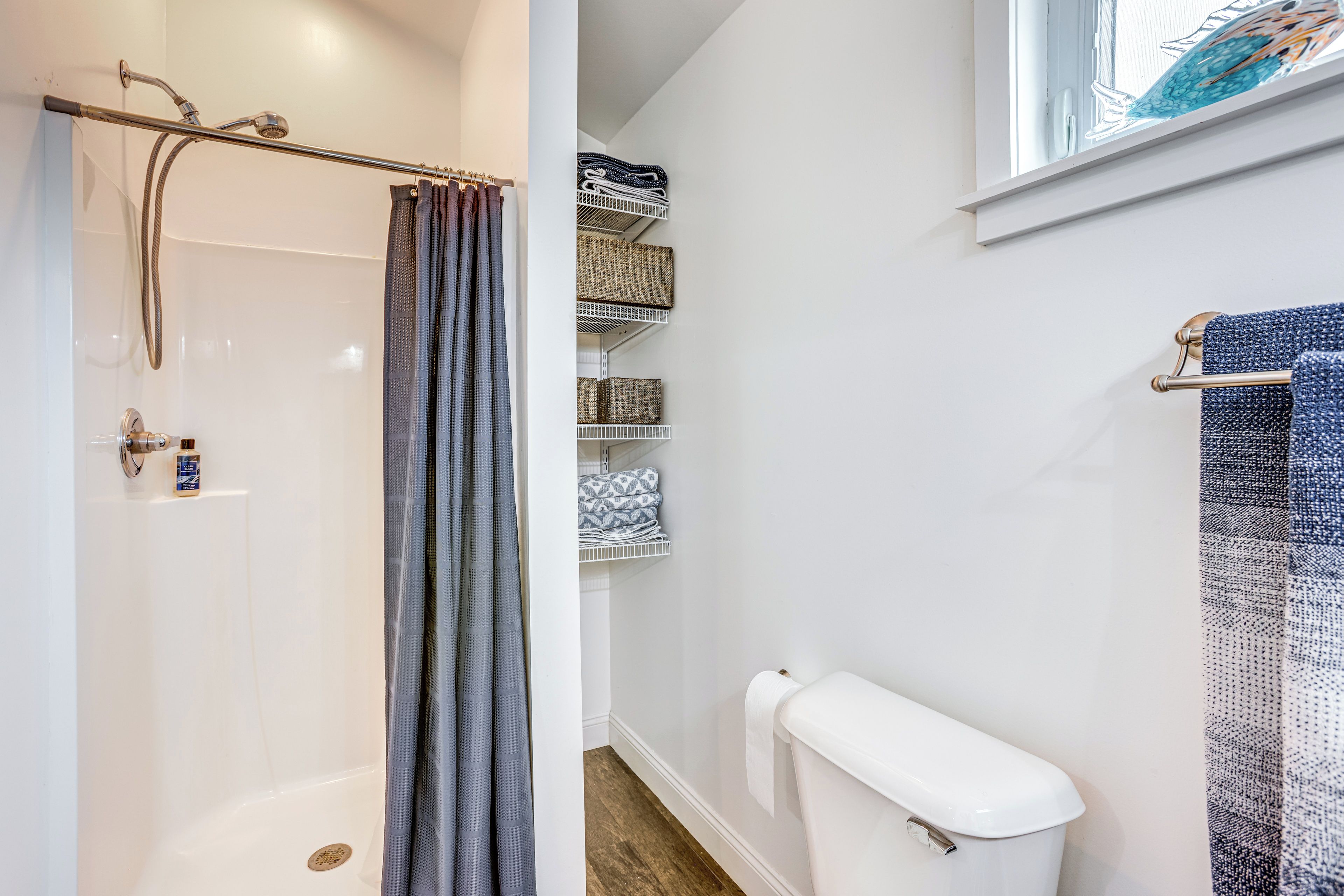 A bathroom with a shower, toilet, and storage shelves.