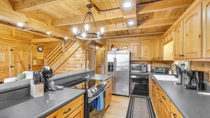 A wooden cabin interior with a kitchen featuring a large island, stainless steel appliances, and a wooden staircase.