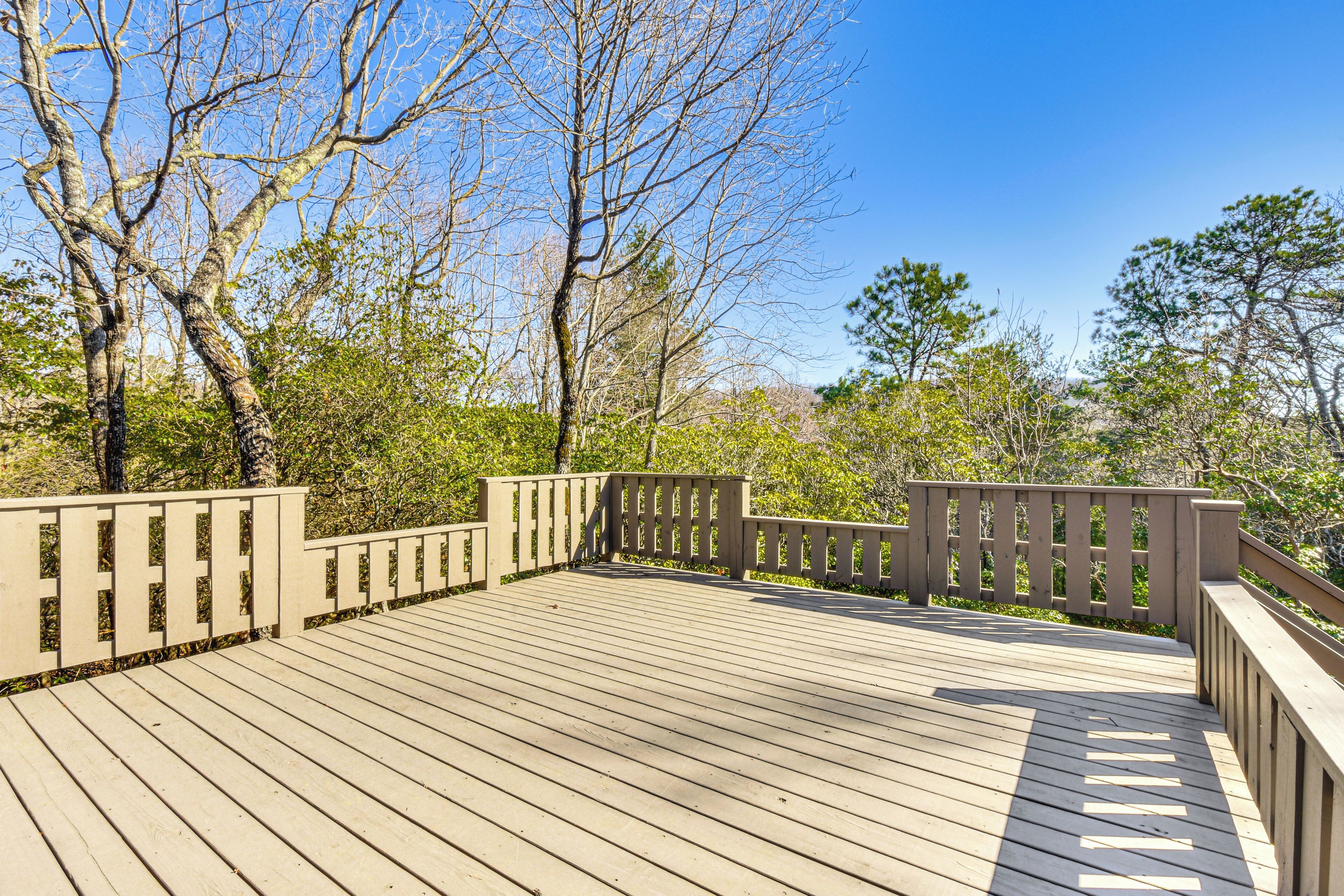 A wooden deck with railings, surrounded by trees and greenery.