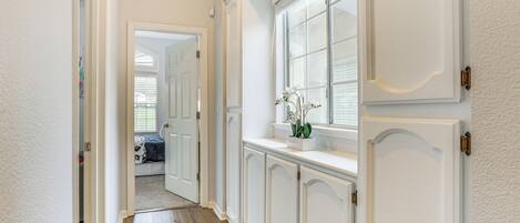 Un pasillo con paredes blancas, suelo de madera y una ventana con cortinas blancas.