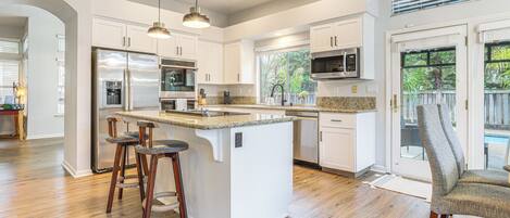A modern kitchen with white cabinetry, stainless steel appliances, and a central island with bar stools.
