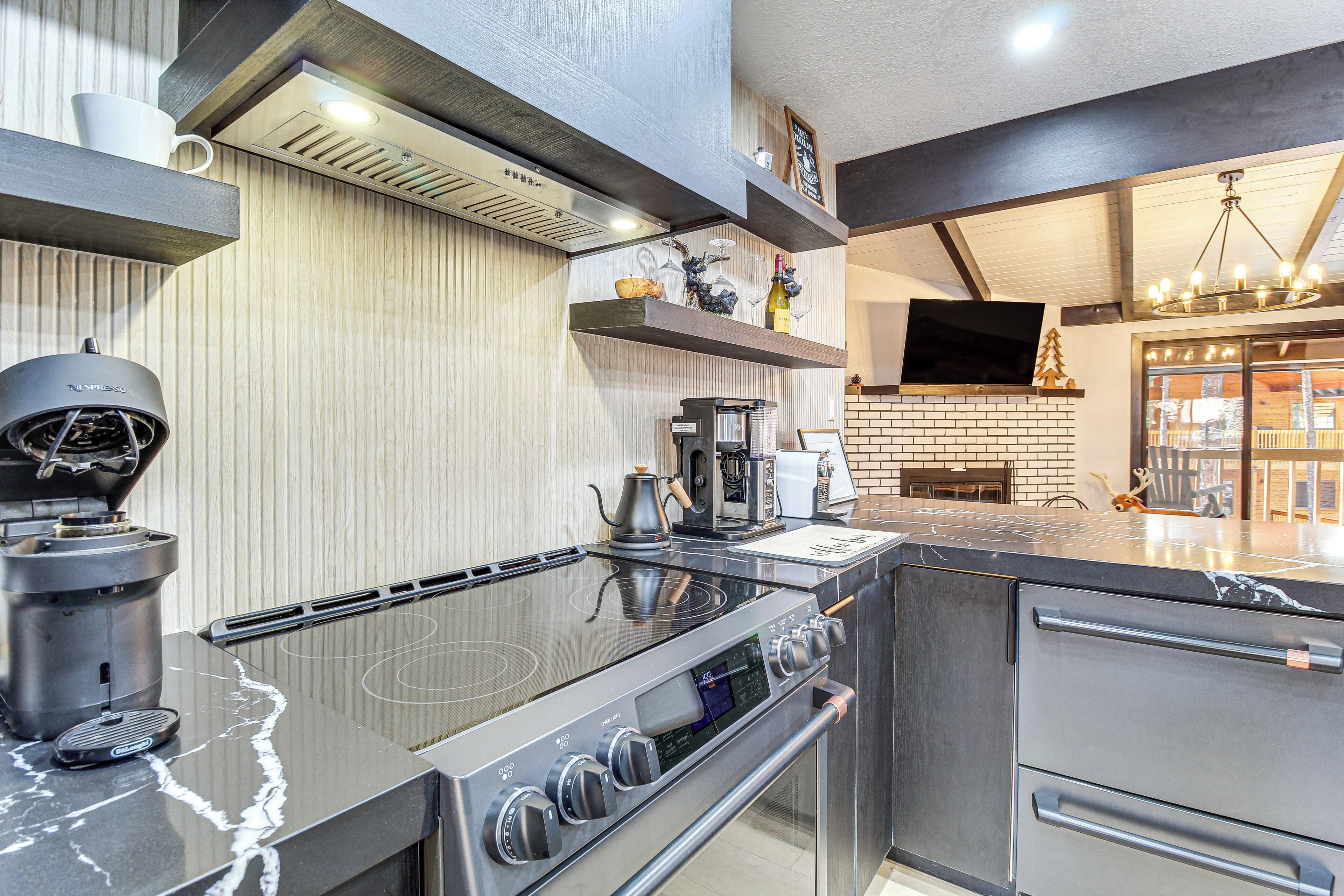 Una cocina moderna con estufa de acero inoxidable, cafetera y televisor de pantalla plana sobre la encimera.
