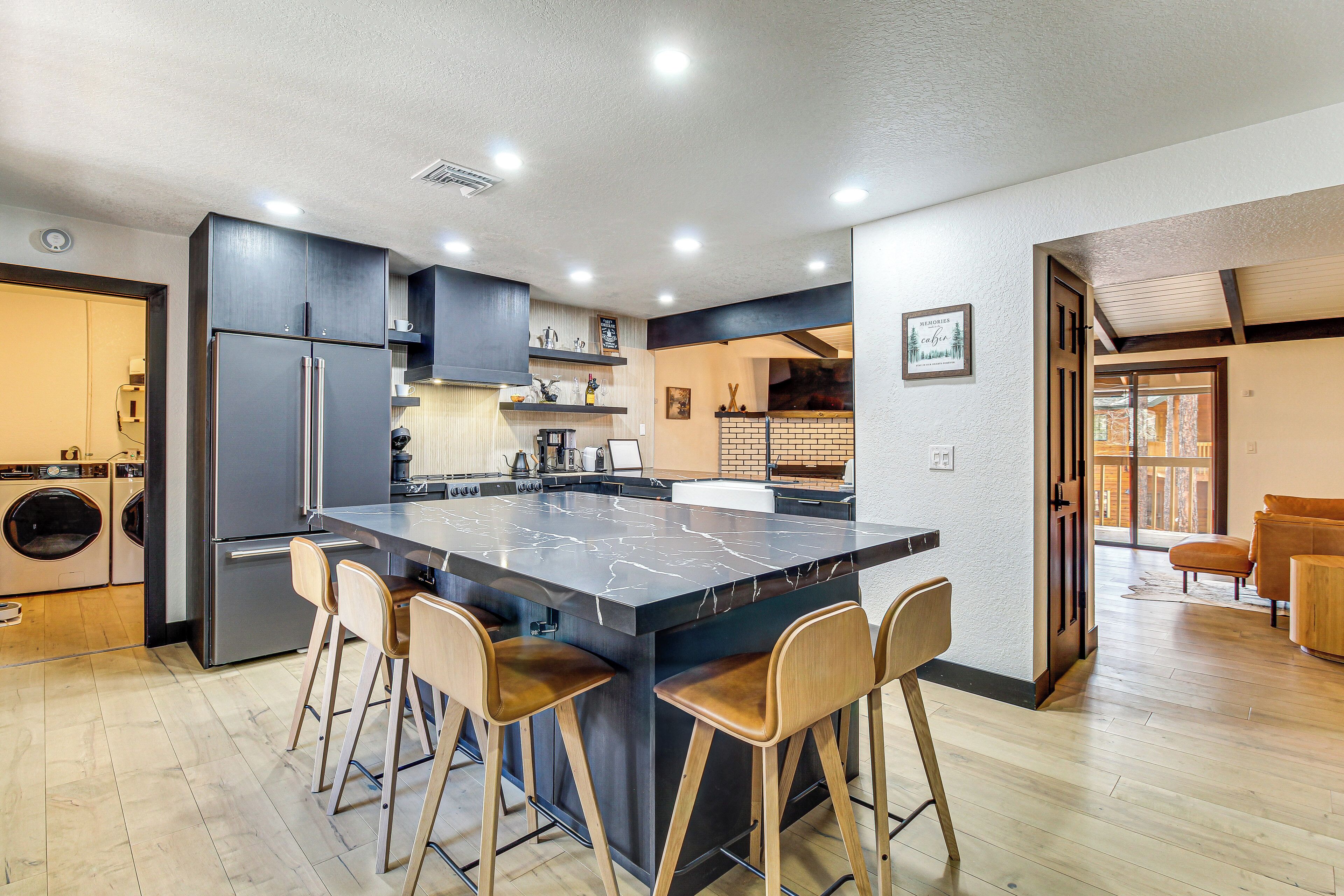 A modern kitchen with a central island, bar stools, stainless steel appliances, and a laundry area.