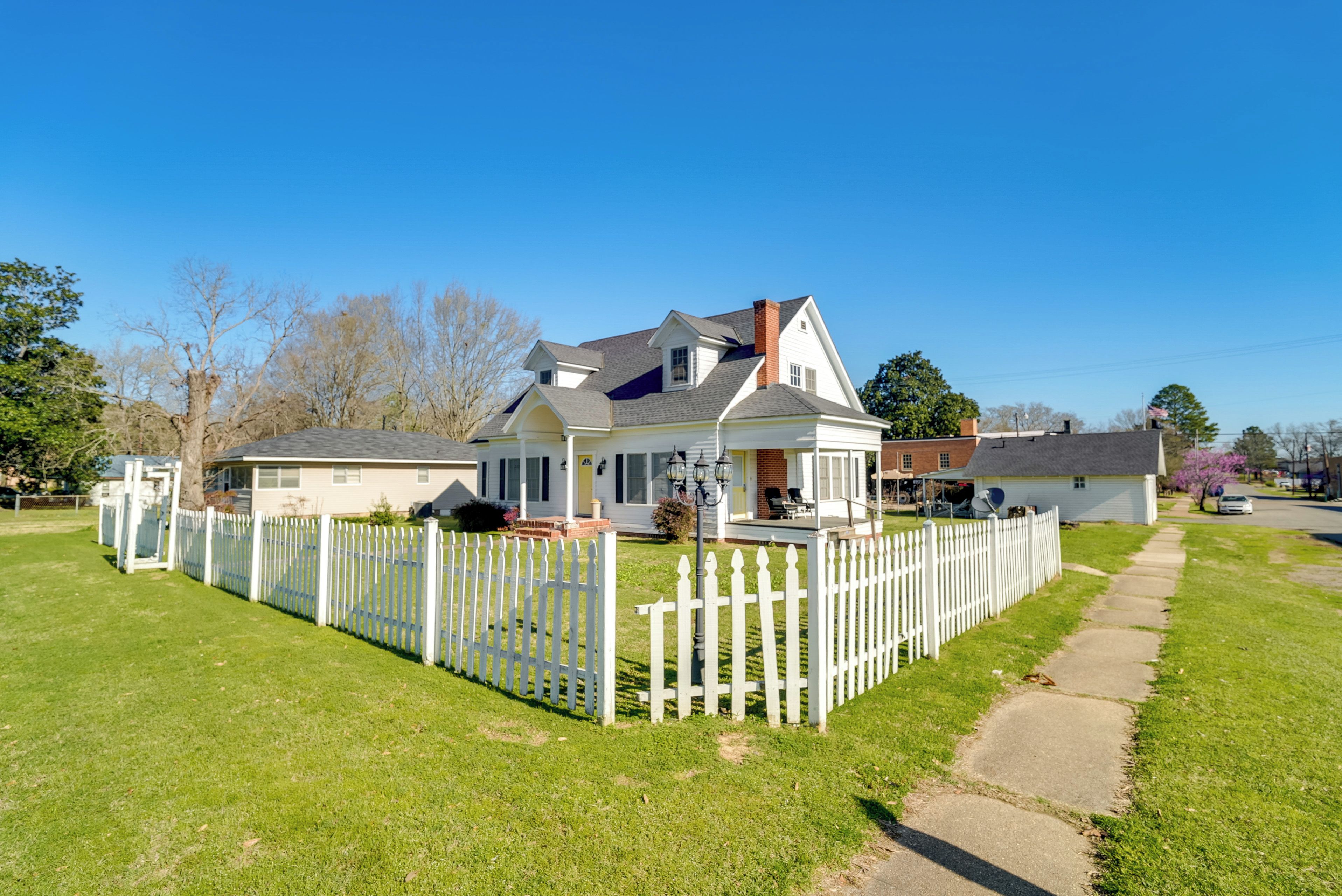 A two-story house with a white picket fence, a front porch, and a driveway leading to a garage.