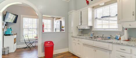 A kitchen with white cabinets, a granite countertop, and a red trash bin.