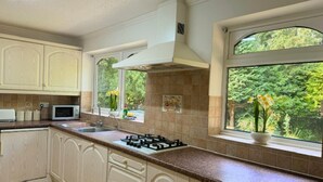 Una cocina con armarios blancos, microondas, cocina a gas y ventana con vista a follaje.