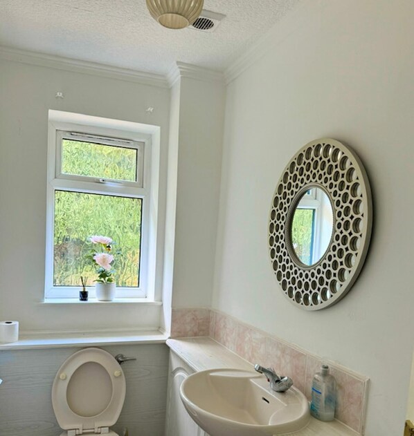 Un baño con inodoro, lavamanos y ventana con vistas a la vegetación.