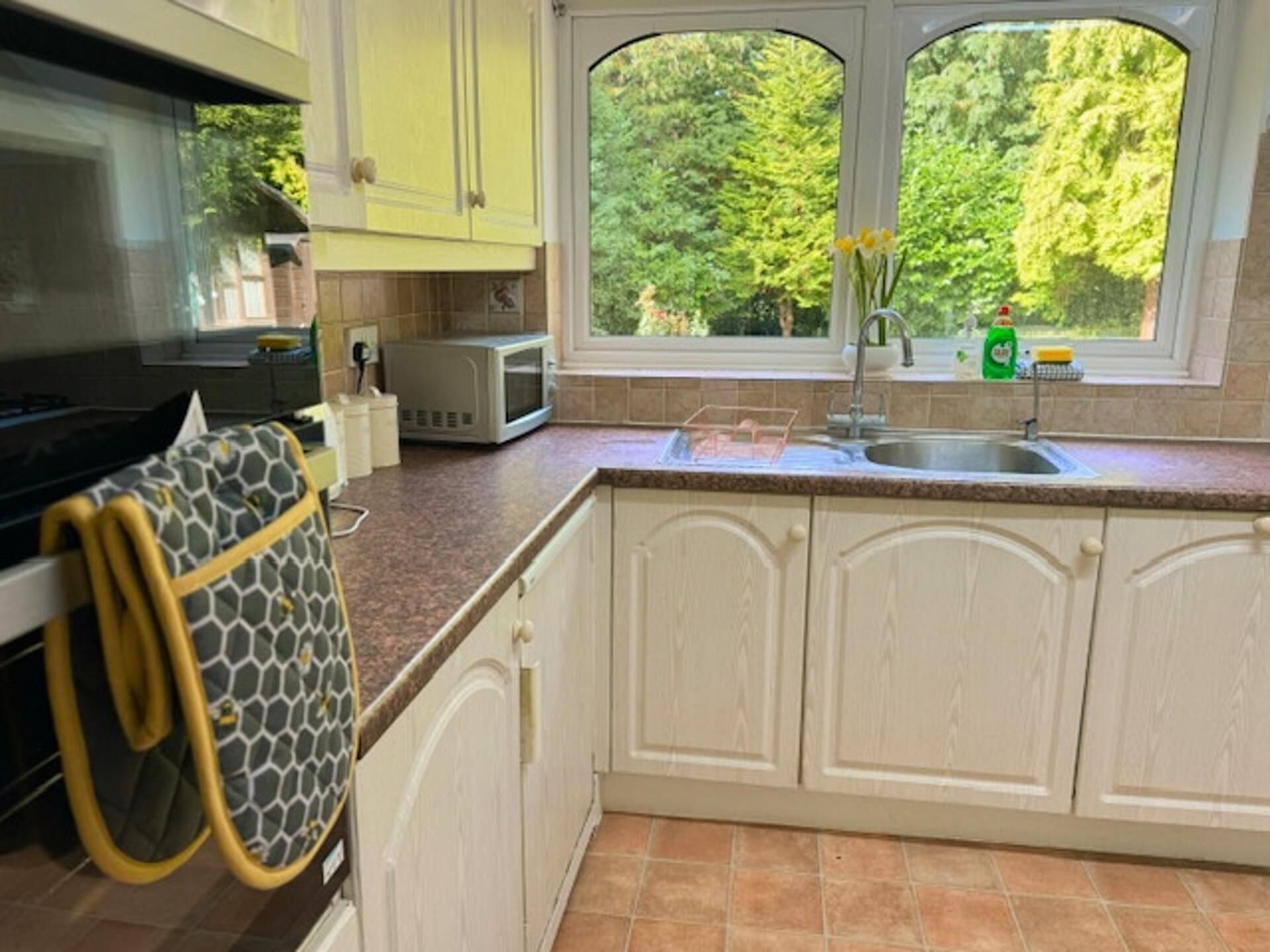 A kitchen with white cabinets, a microwave, a sink, and a window with a view of trees.