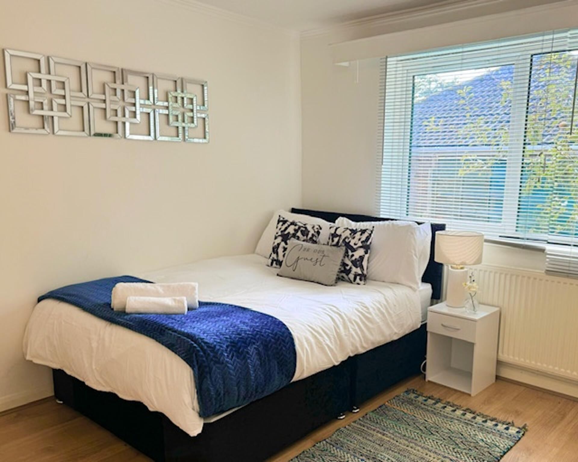 A bedroom with a bed, a bedside table, a lamp, and a window with blinds.