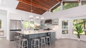 Una cocina moderna con una isla grande, electrodomésticos de acero inoxidable y techo de madera.
