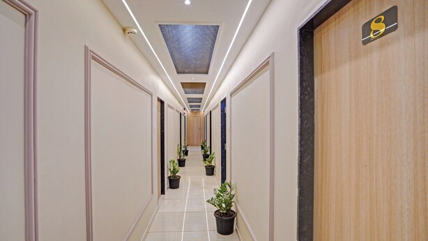 En hotelgang med moderne design, der viser en lang korridor med potteplanter, en trædør til højre og et loft med indbyggede lys.