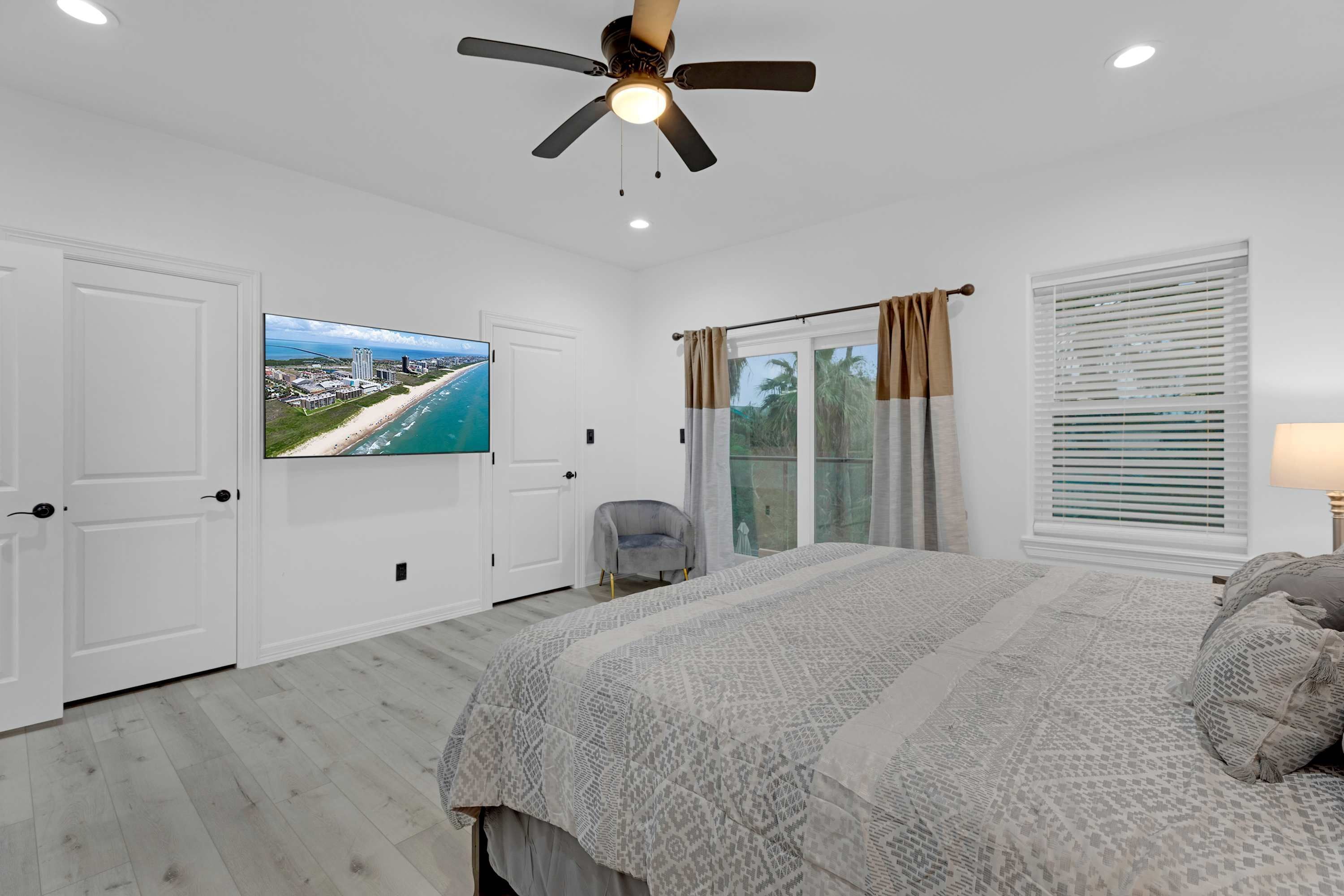 A bedroom with a bed, a ceiling fan, a TV, a chair, and a window with blinds.