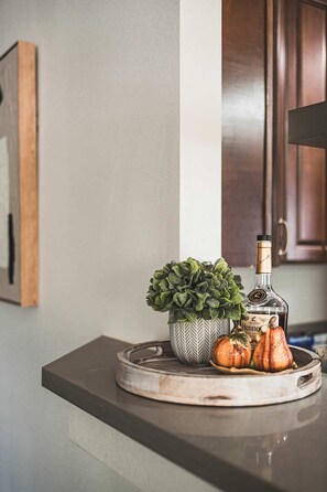 A kitchen counter with a decorative plant, a bottle, and carved pumpkins.