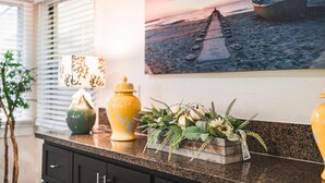 Een aanrecht met decoratieve voorwerpen, een schilderij van een strandlandschap en een plant in pot.