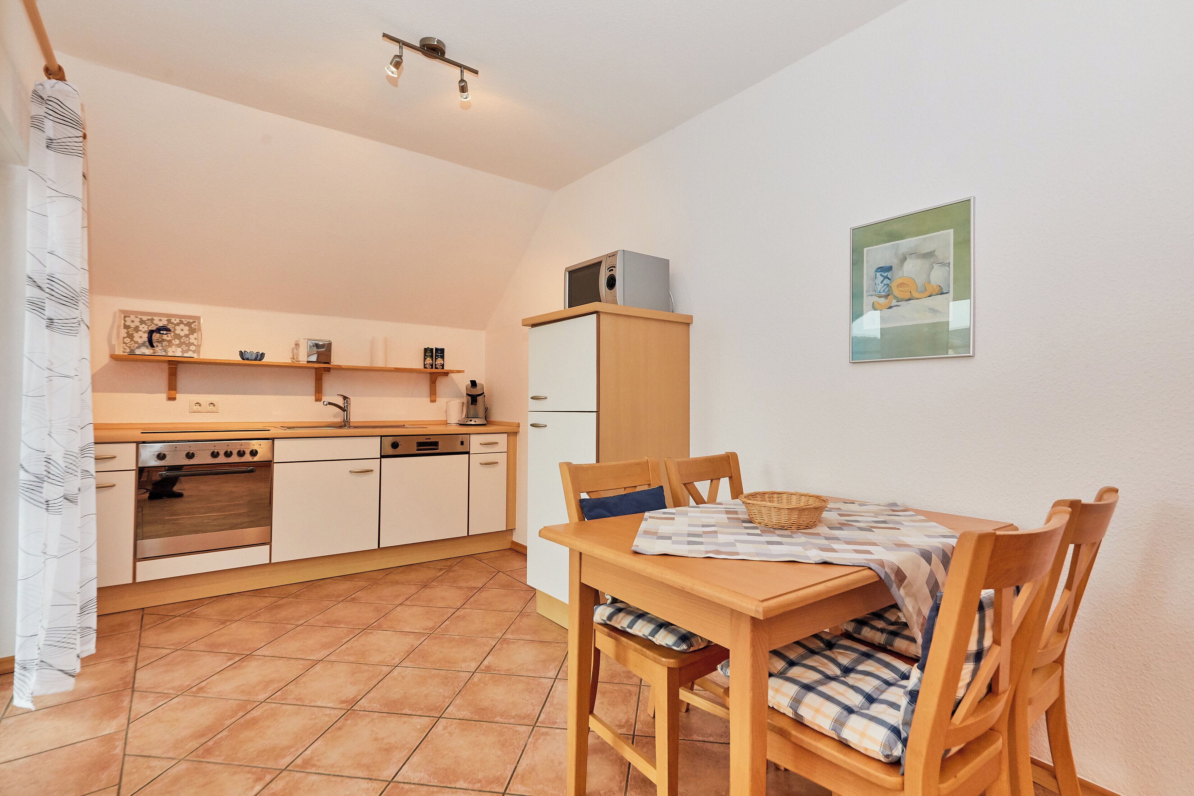 Eine kleine Küche mit einem Holztisch und Stühlen, einer Mikrowelle auf einem Schrank und einem Bild an der Wand.