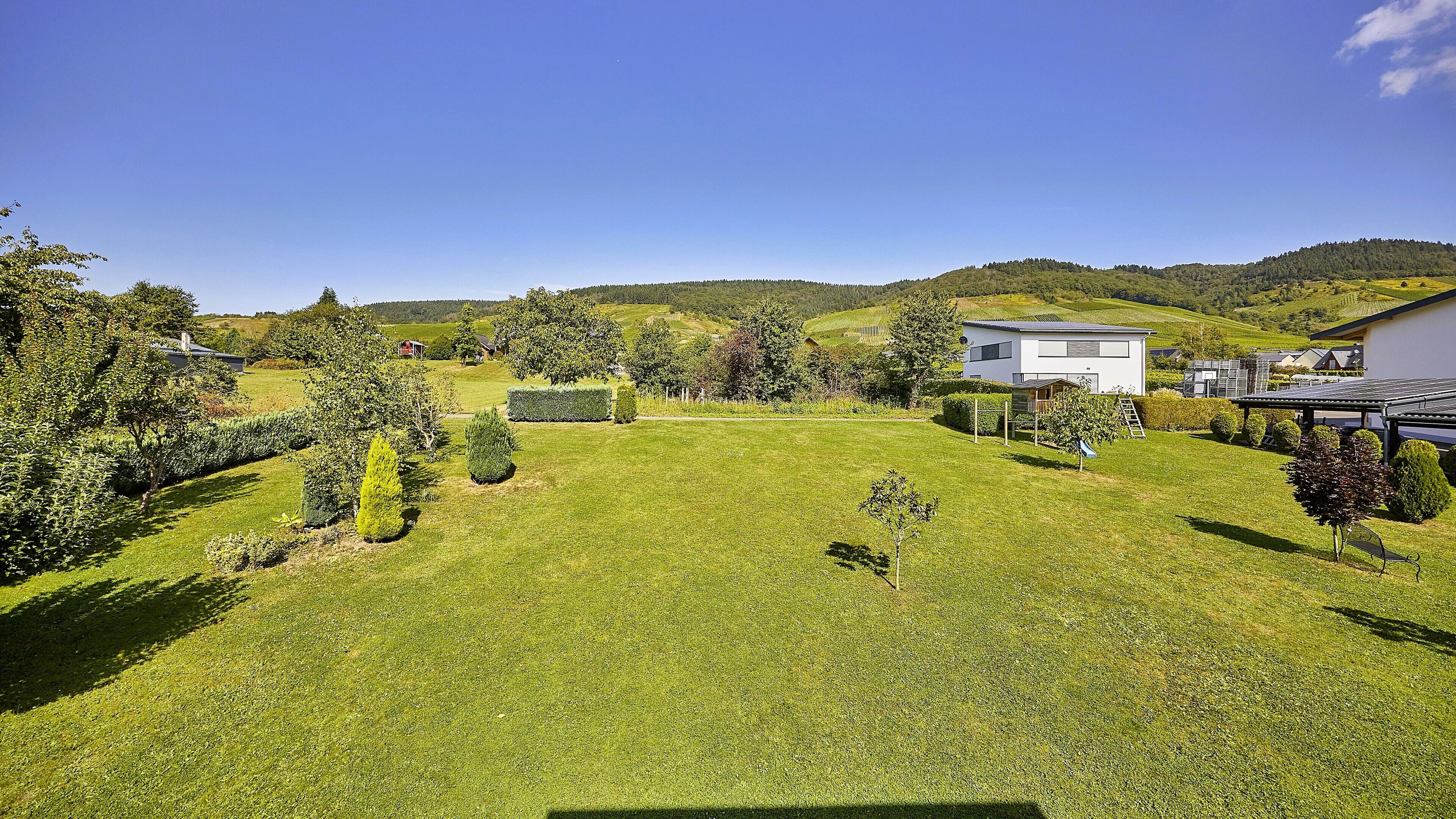 A residential area with a well-maintained lawn, a modern house with a flat roof, and a clear sky.