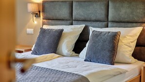 A neatly made bed with a grey headboard, a bedside lamp, and a power outlet on the wall.