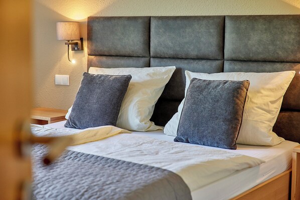 A neatly made bed with a grey headboard, a bedside lamp, and a power outlet on the wall. - Gut Hermes (Kröv)