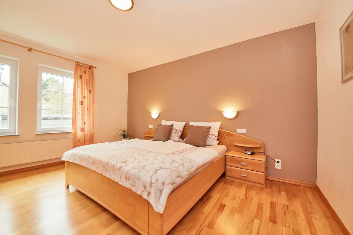 A bedroom with a wooden bed, bedside tables, a nightstand, and a window with curtains.