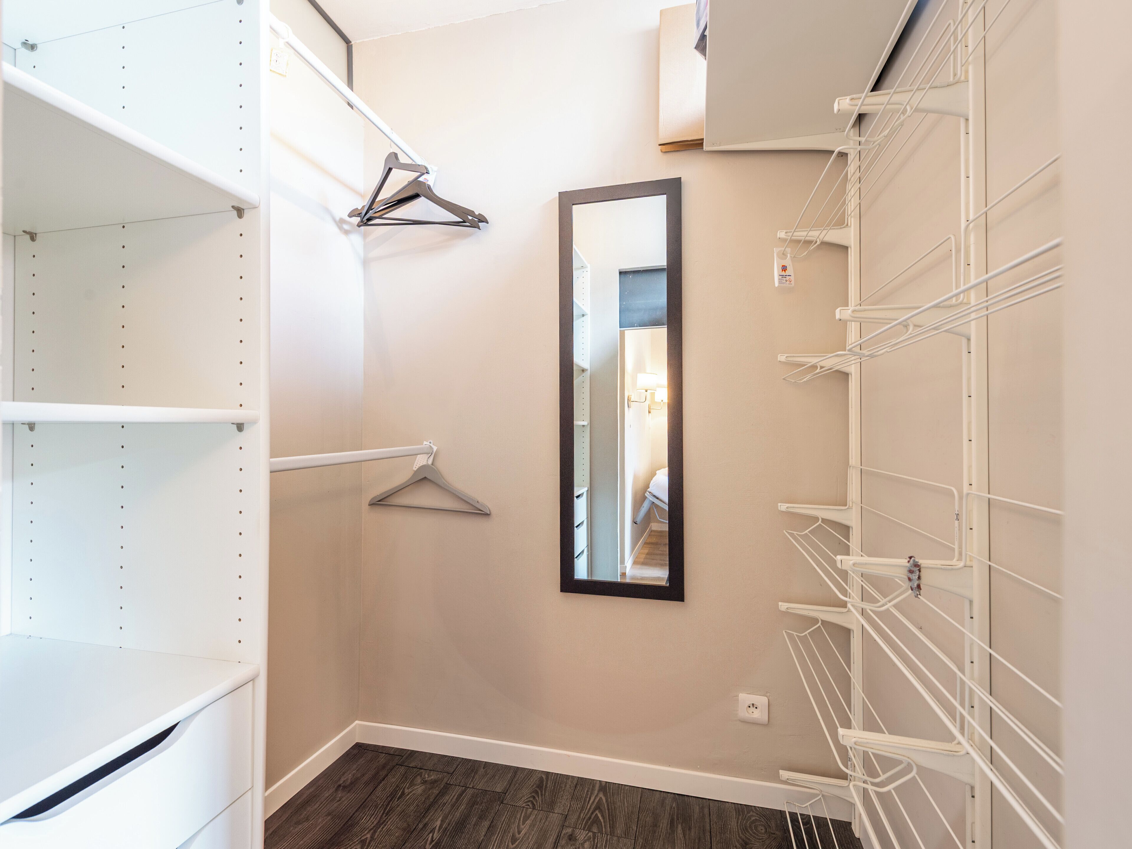 A walk-in closet with open shelving, a mirror, and a white metal drying rack.