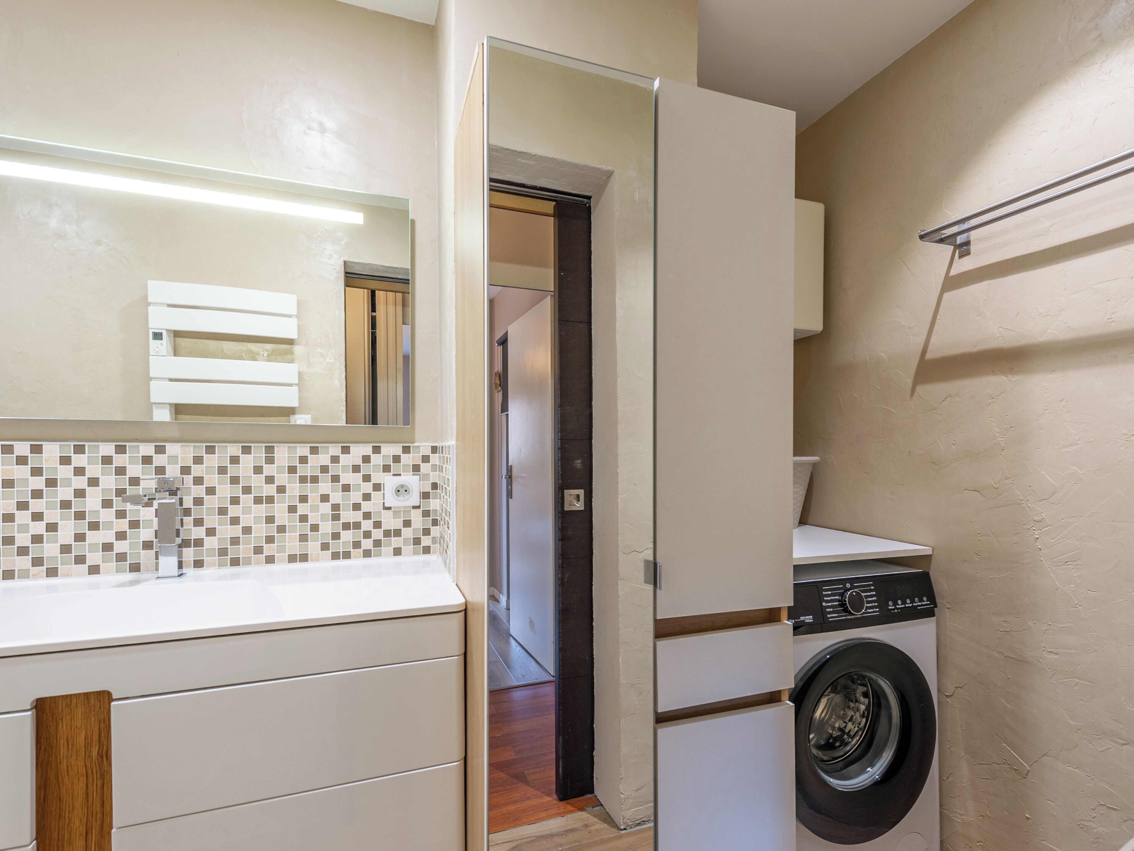 A compact laundry room with a washing machine, a tiled backsplash, and a mirror above the sink.