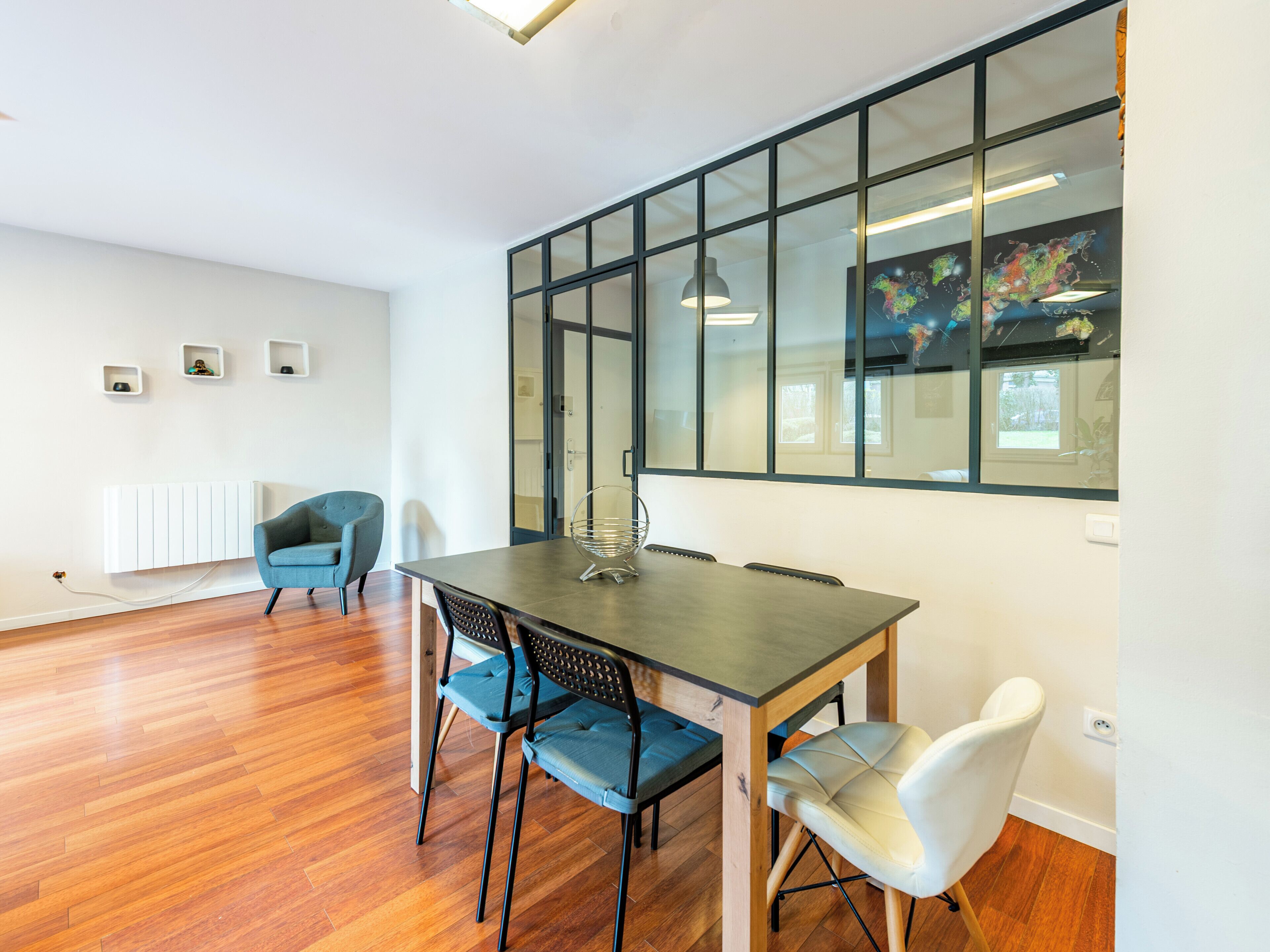 A modern dining area with a wooden table and chairs, a radiator, and a large window with a view of a map.