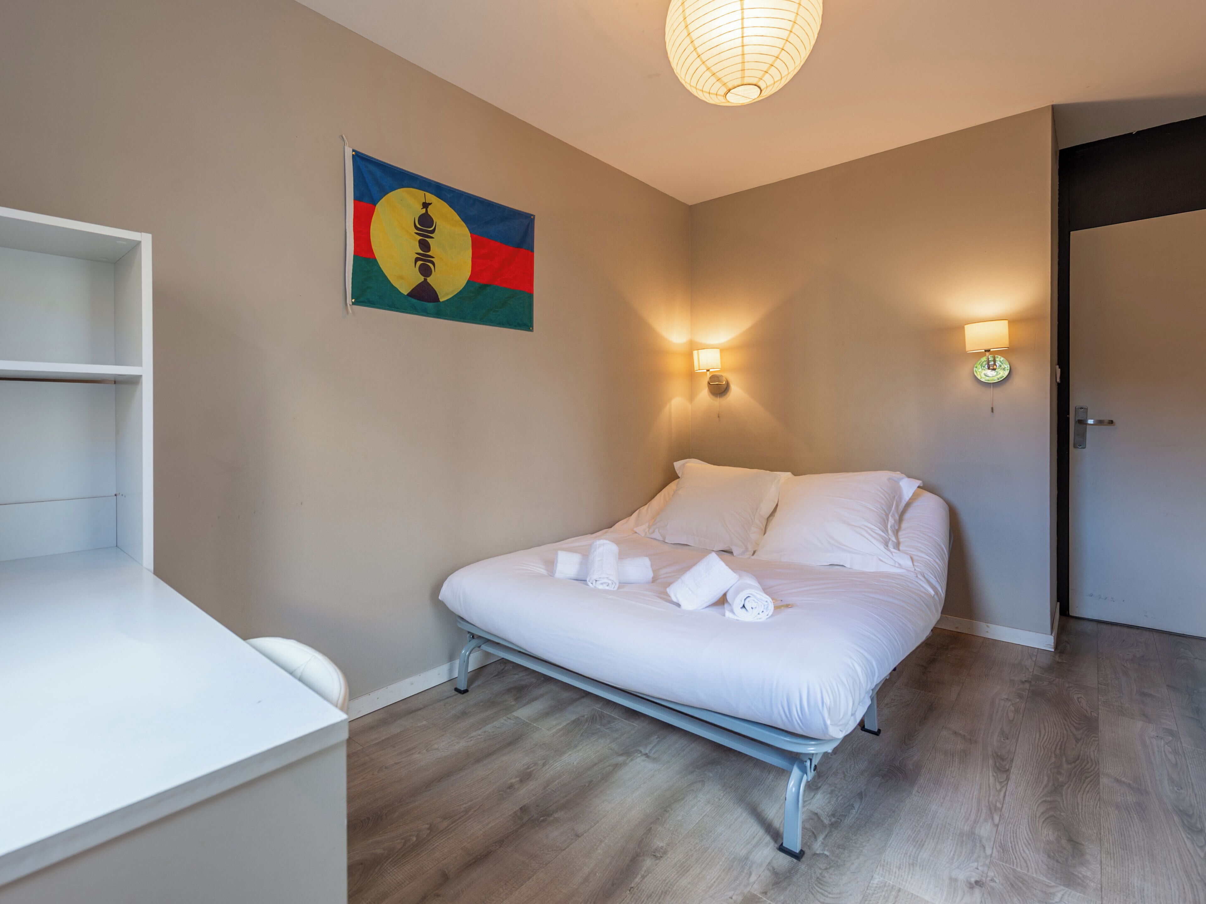 A bedroom with a bed, bedside lamps, a wall-mounted artwork, and a wooden floor.