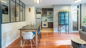A modern kitchen with a dining area, wooden flooring, and a view through a large window.