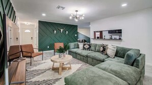 A modern living room with a sectional sofa, a round coffee table, and a mirror above a kitchen counter.