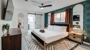 A modern bedroom with a bed, a nightstand, a dresser, a ceiling fan, and a large window with curtains.