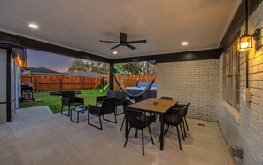 A covered patio area with a table and chairs, a hammock, and a hot tub.