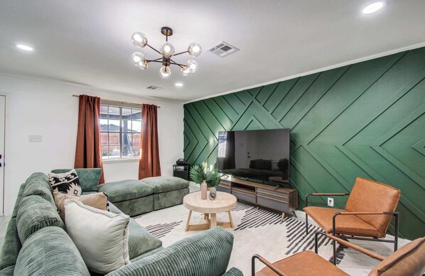 A modern living room with a green accent wall, a sofa set, a coffee table, and a TV.