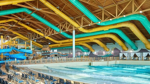 An indoor swimming pool with multiple lanes, a wooden ceiling structure, and a seating area with chairs.