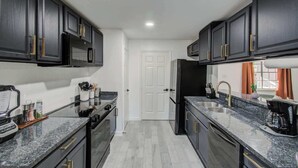 A modern kitchen with dark cabinetry, granite countertops, and stainless steel appliances.