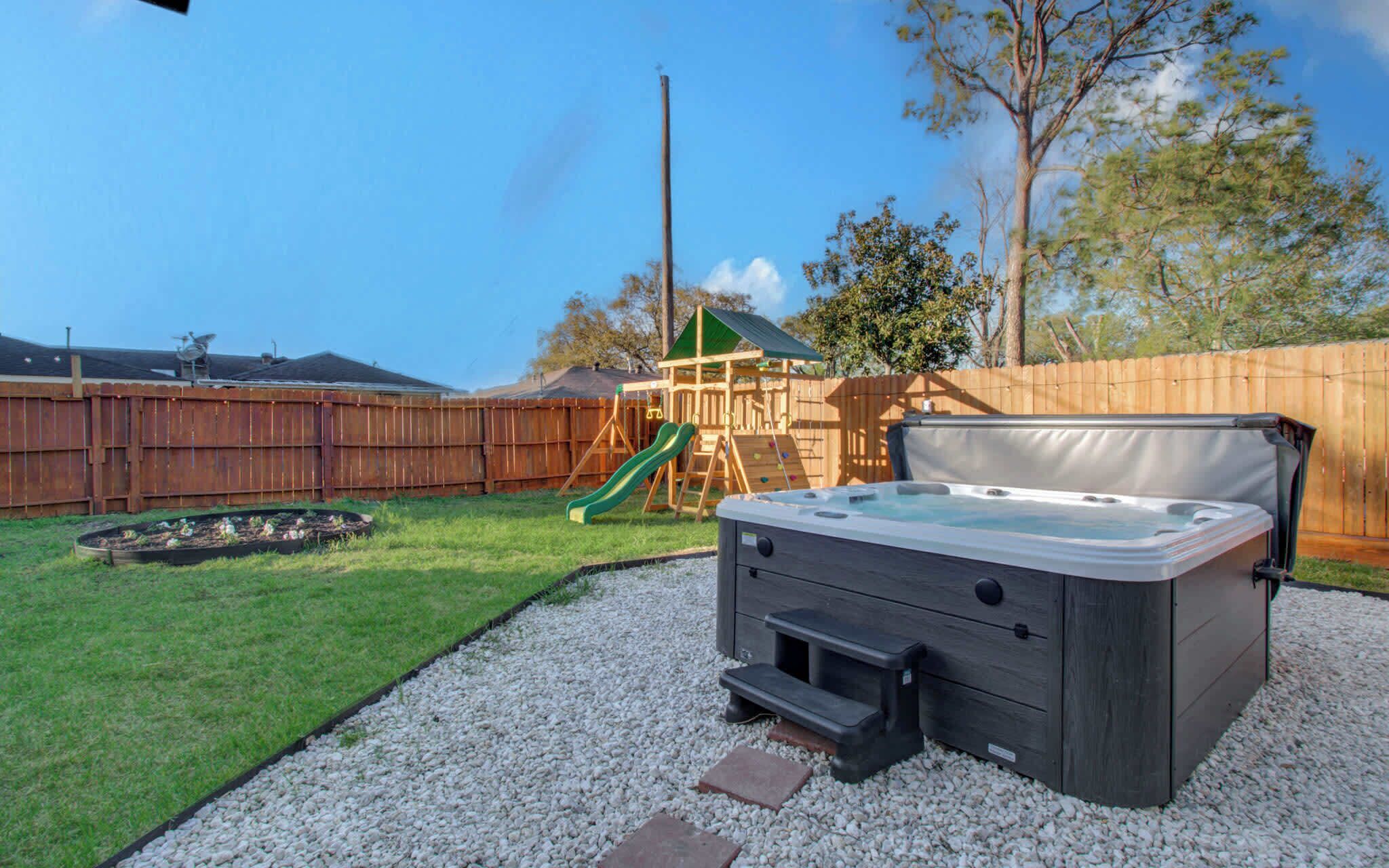 A backyard with a hot tub, a wooden play structure, and a wooden fence.