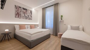 Een moderne hotelkamer met een groot bed, een kleiner bed, een nachtkastje met een lamp, een wanddecoratie en een raam met gordijnen.