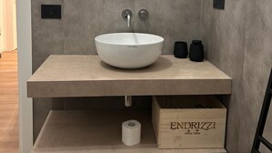 Een moderne badkamer met een ronde spiegel, een witte wastafel en een houten doos met de tekst 'ENDRIZZI'.