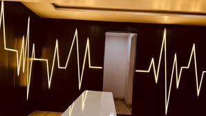 Una habitación de hotel moderna con una amplia mesa blanca, paredes de madera oscura e instalación de luces única en el techo.