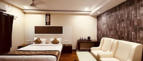 A modern hotel room with a large bed, a sofa, a coffee table, and a wooden accent wall.