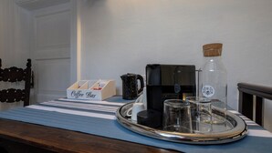 Disposição de um bar de café com bandeja, cafeteira, caneca e recipientes de vidro sobre uma toalha de mesa listrada.