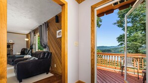 Ein gemütliches Zimmer mit Holzbalkendecke, einem schwarzen Leder-Sofa und Blick auf eine Terrasse mit Gartenmöbeln.